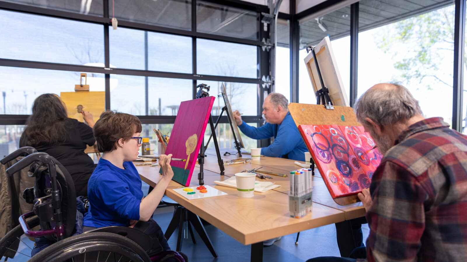 A group of elderly and young people sitting at a table painting together.