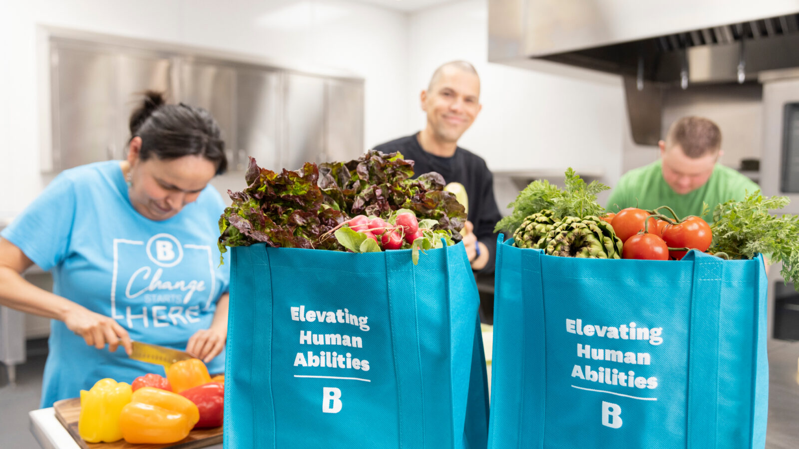 People in a professional kitchen cutting peppers and other vegetables.
