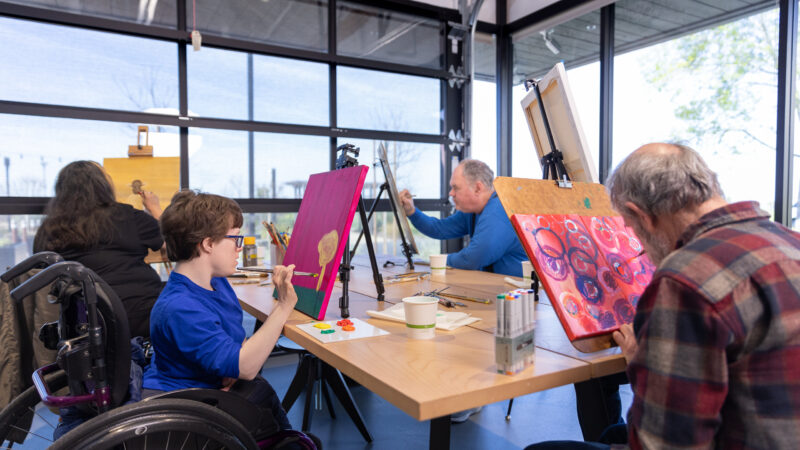 A group of elderly and young people sitting at a table painting together.